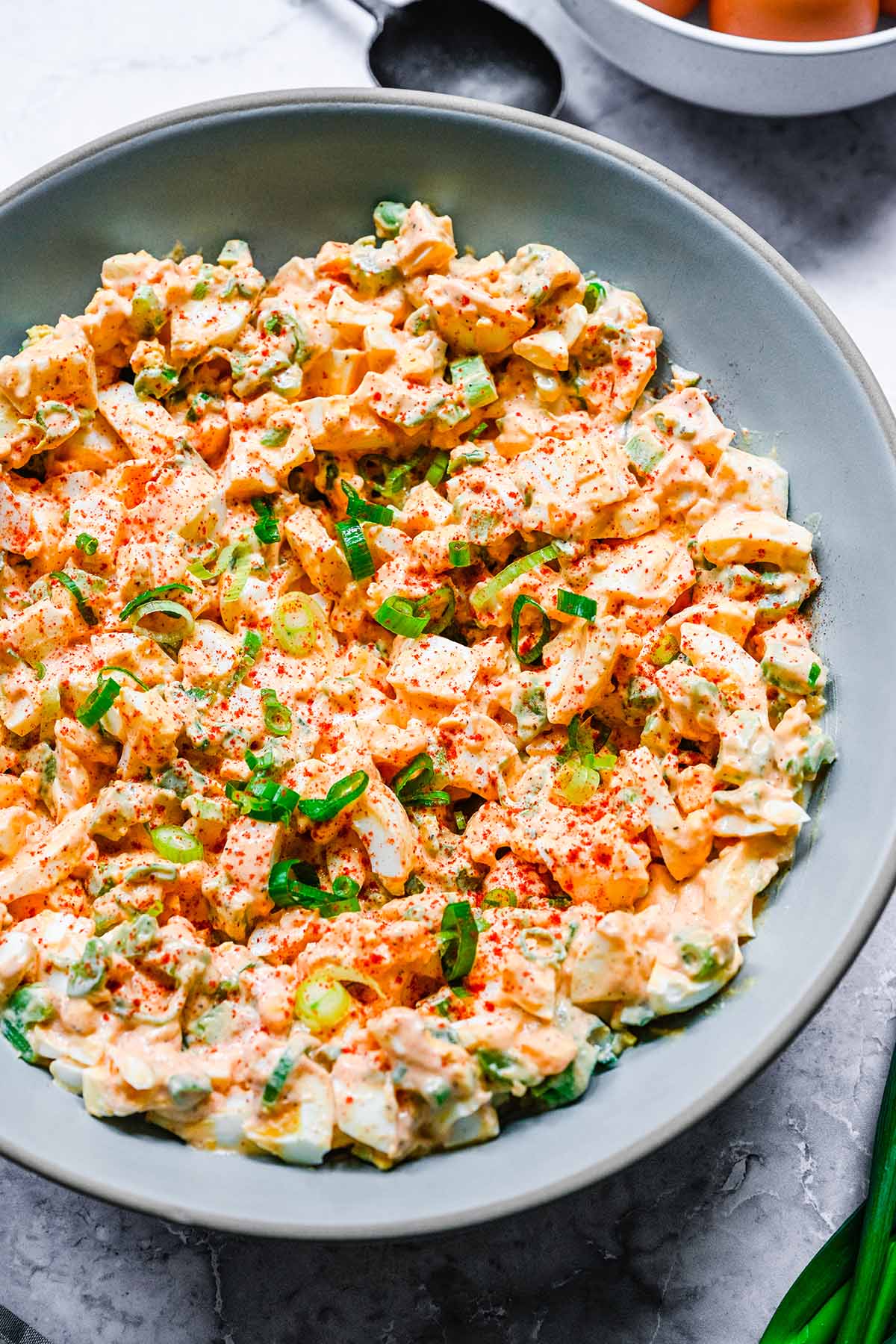A close up view of Deviled Egg Salad in a shallow blue-grey bowl, garnished with sliced green onion and paprika.