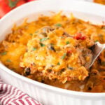 A serving of Chicken Taco Casserole on a spatula being held over the rest of the casserole in a white dish.
