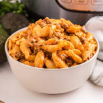 Taco Pasta piled high in a white bowl, sitting in front of an Instant Pot.