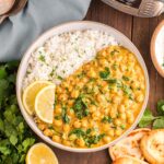 Instant Pot Chickpea Curry plated with rice, lemon slices and chopped cilantro in a beige bowl, viewed from overhead.