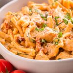 A closeup of Marry Me Chicken Pasta in a white bowl garnished with finely grated parmesan and sliced fresh basil.