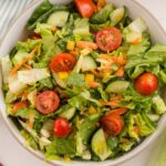 Romaine Lettuce Salad in an off-white bowl next to a blue and white striped linen and bronze forks, showing the sliced cherry tomatoes, shredded carrot and diced yellow bell pepper nestled in the lettuce.