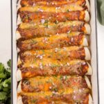 Rotisserie Chicken Enchiladas viewed from overhead in a white casserole dish that has a black rim, next to onion and cilantro garnishes and a green linen.