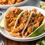 Instant Pot Salsa Chicken served in three soft flour tortillas on a stack of two white plates, with lime wedges propping them up on both sides.