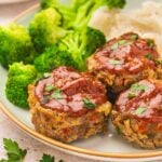 Three Mini Meatloaves on a white plate with gold trim, served with steamed broccoli and creamy mashed potatoes.
