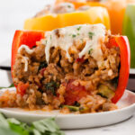 A red bell pepper stuffed with a rice and sausage mixture, and topped with melted mozzarella, sliced open through the middle to show the filling.