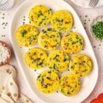 Ten Cottage Cheese Egg Bites served on a white oval platter, garnished with chopped fresh chives, viewed from overhead.