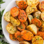 Roasted carrots and potatoes garnished with finely chopped fresh parsley piled onto a curved white plate, viewed from overhead.