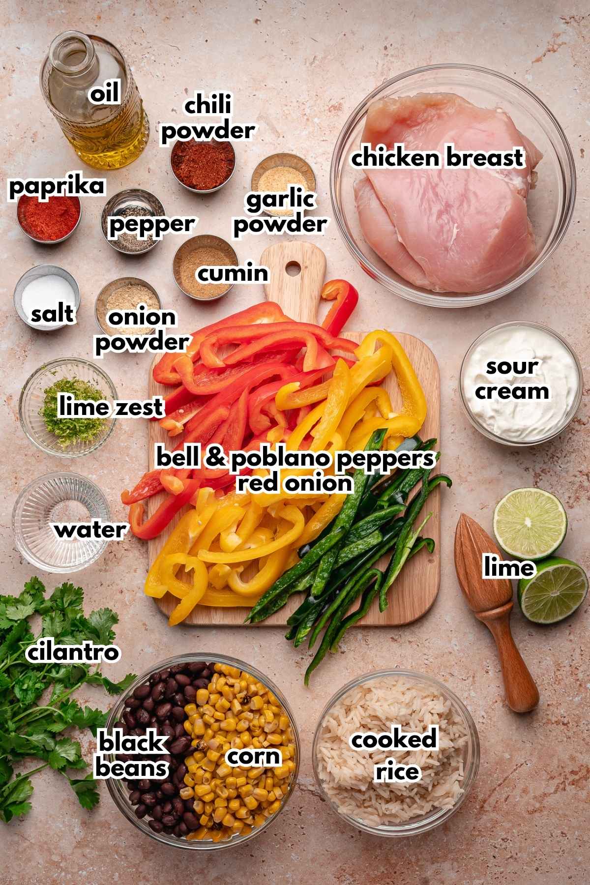 Labeled ingredients for chicken fajita bowls, including raw chicken breast, sliced peppers, spices, rice, black beans, corn, and sour cream.