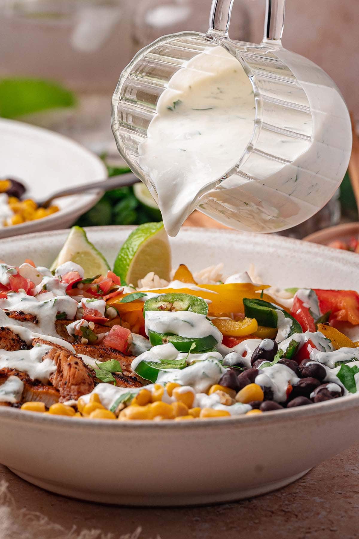 Cilantro lime crema poured from a glass pitcher over a chicken fajita bowl.
