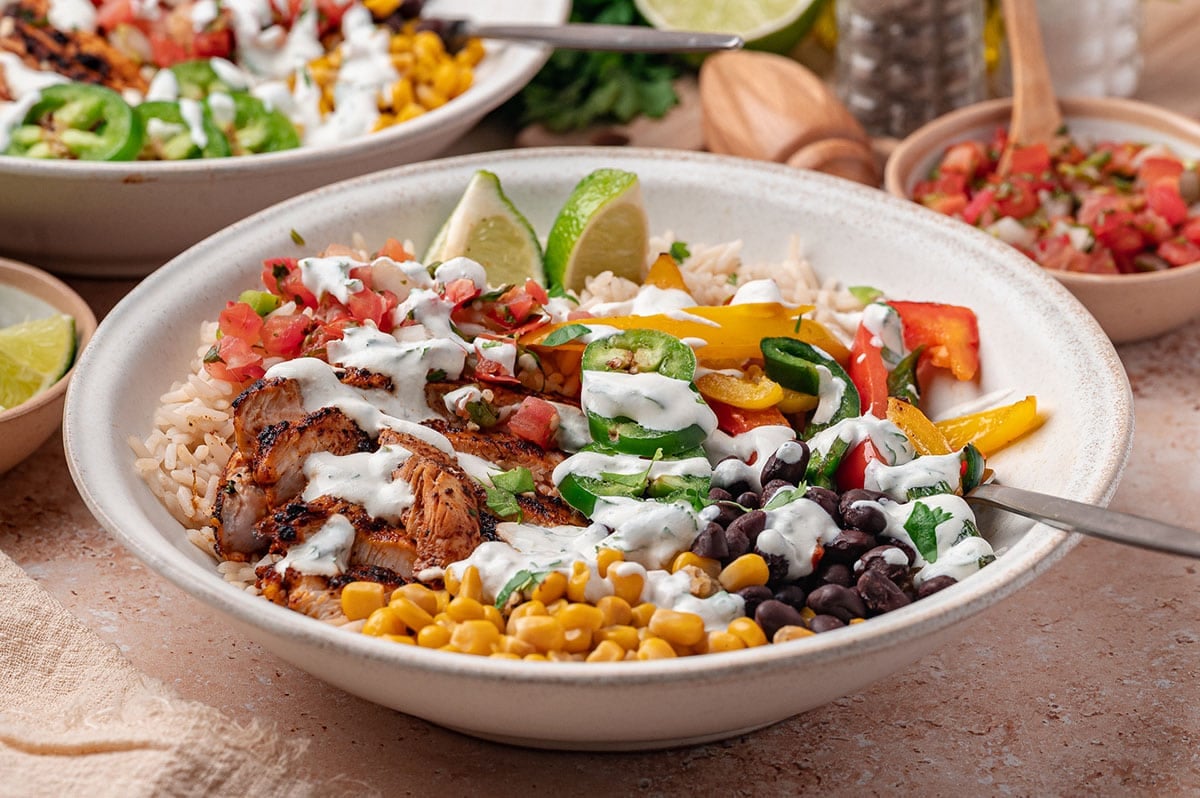 Side view of a chicken fajita bowl drizzled with cilantro lime crema, with a second bowl behind it.