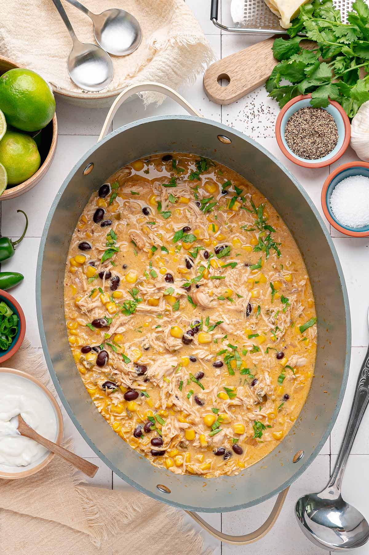 Overhead view of creamy chicken chili with cilantro, surrounded by limes, sour cream and toppings.