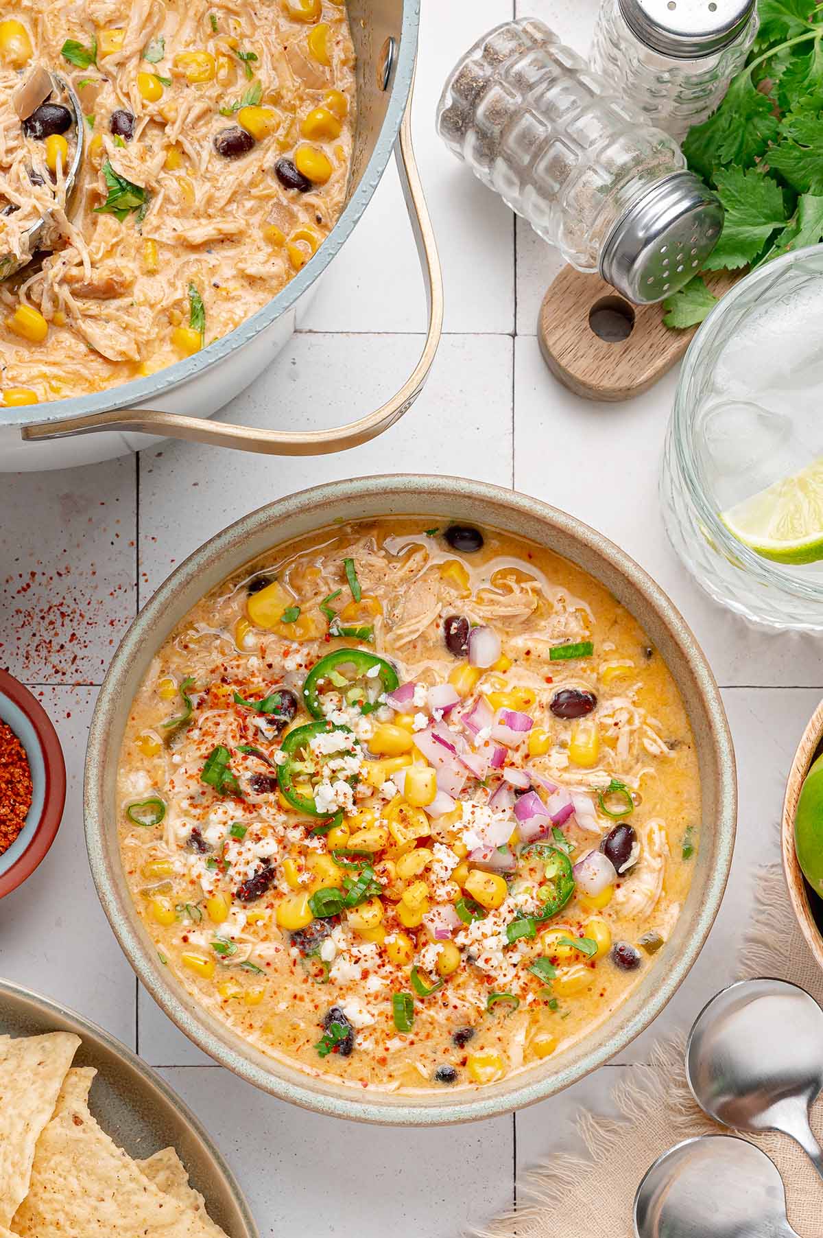Bowl of chicken chili topped with corn, cotija and jalapeño next to the pot it was cooked in.