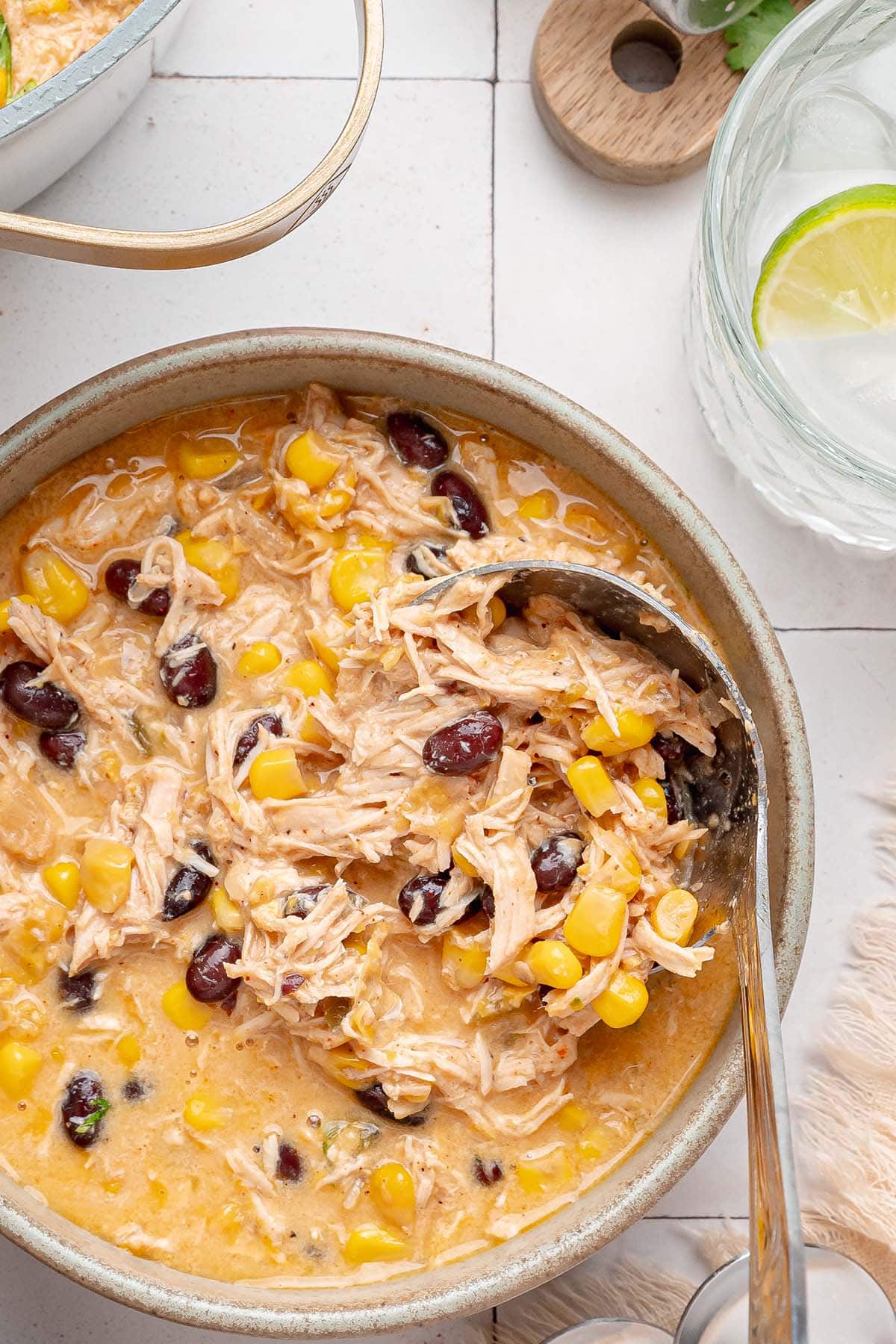 Close up of shredded chicken, sweet corn and black beans in creamy chili with a spoon.