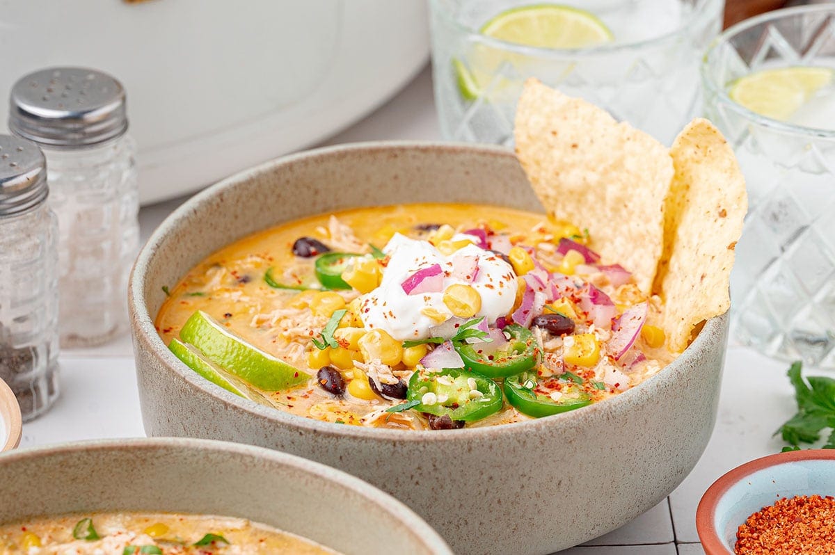 Creamy summer chicken chili in a bowl with sour cream, lime wedges and tortilla chips.