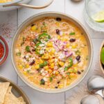 Bowl of slow cooker chicken chili topped with corn, cotija, jalapeño slices and diced red onion.