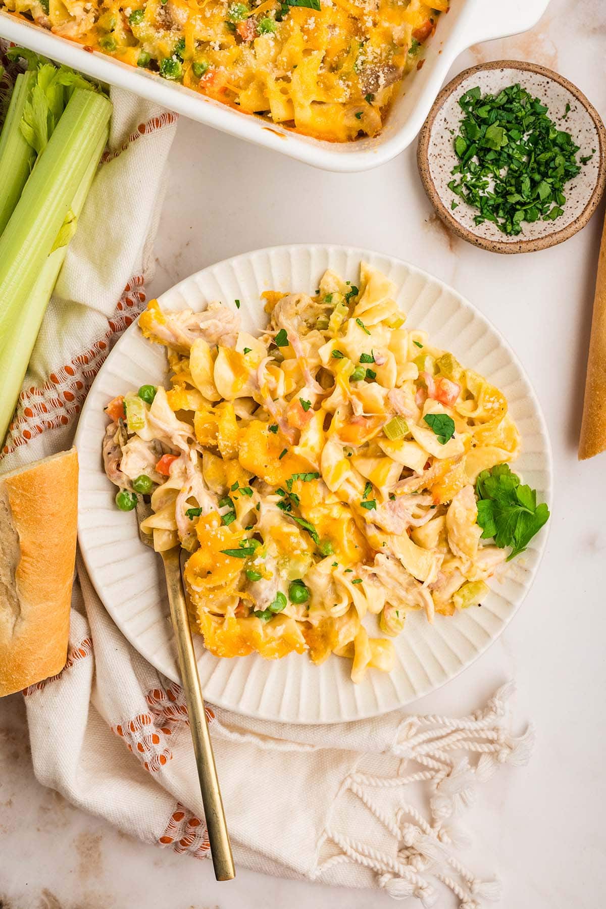 A plate of turkey noodle casserole served with crusty bread, the full baking dish resting nearby.