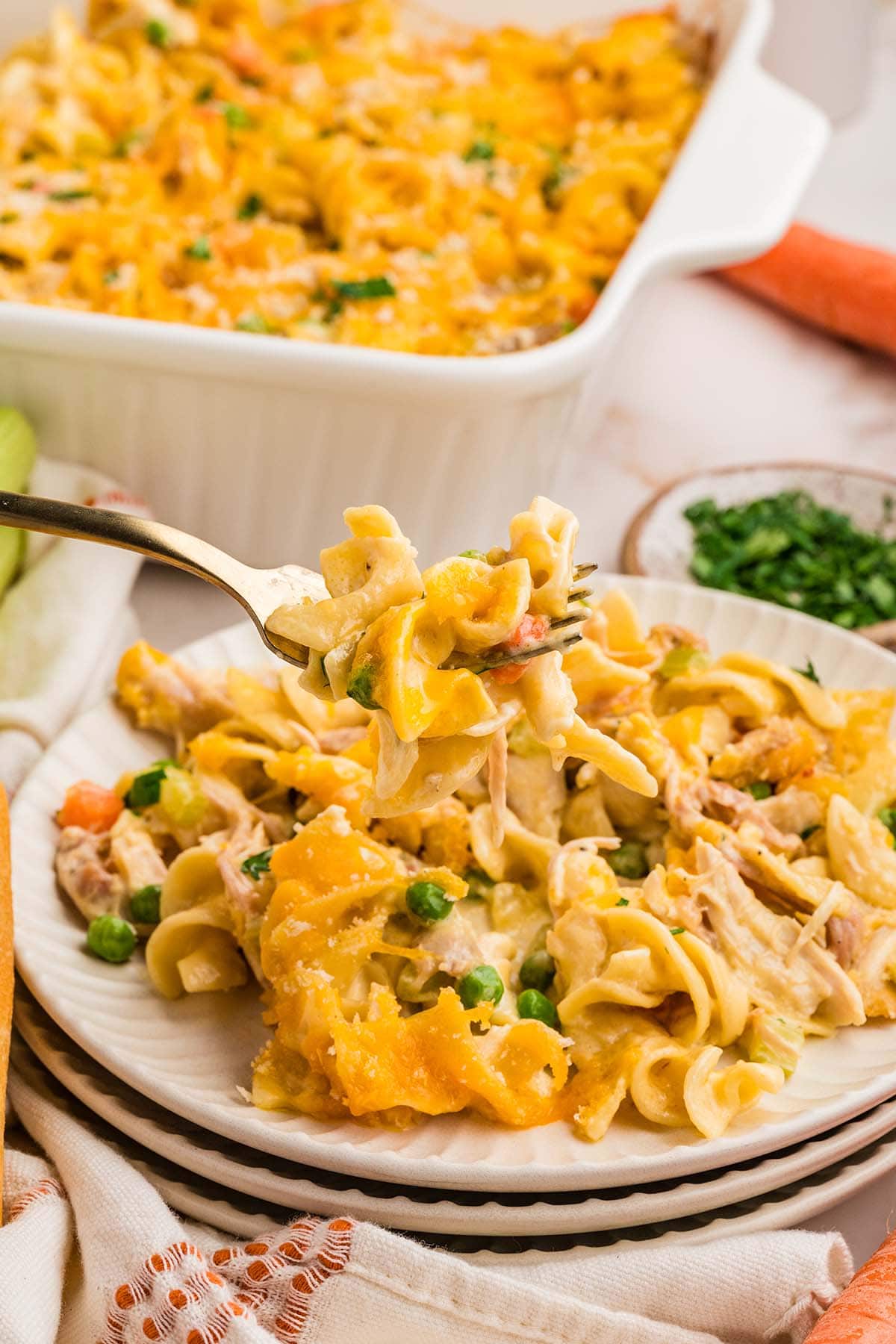A forkful of cheesy turkey noodle casserole lifted from a plate, with the baking dish in the background.