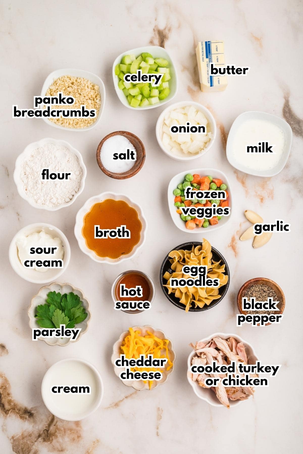 Labelled ingredients for turkey noodle casserole portioned into bowls on a marble surface.