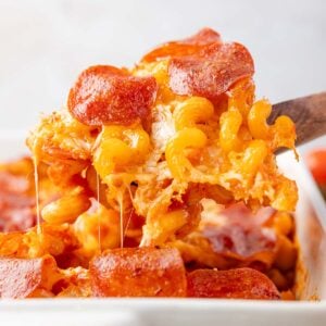 Spoonful of pizza pasta bake with melted cheese pulling from the casserole dish.