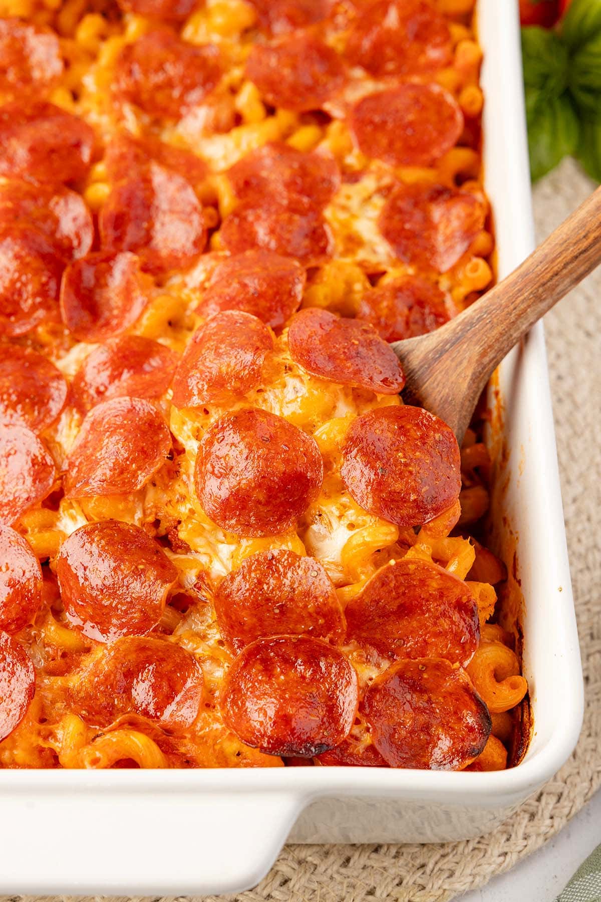 Wooden spoon serving pizza pasta bake from the corner of the casserole dish.