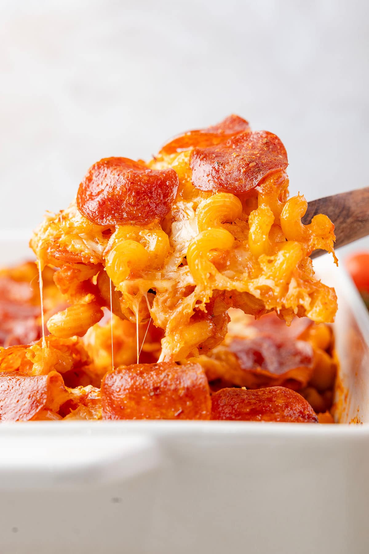 Cheesy spoonful of pizza pasta bake lifted out of the dish with a wooden spoon.