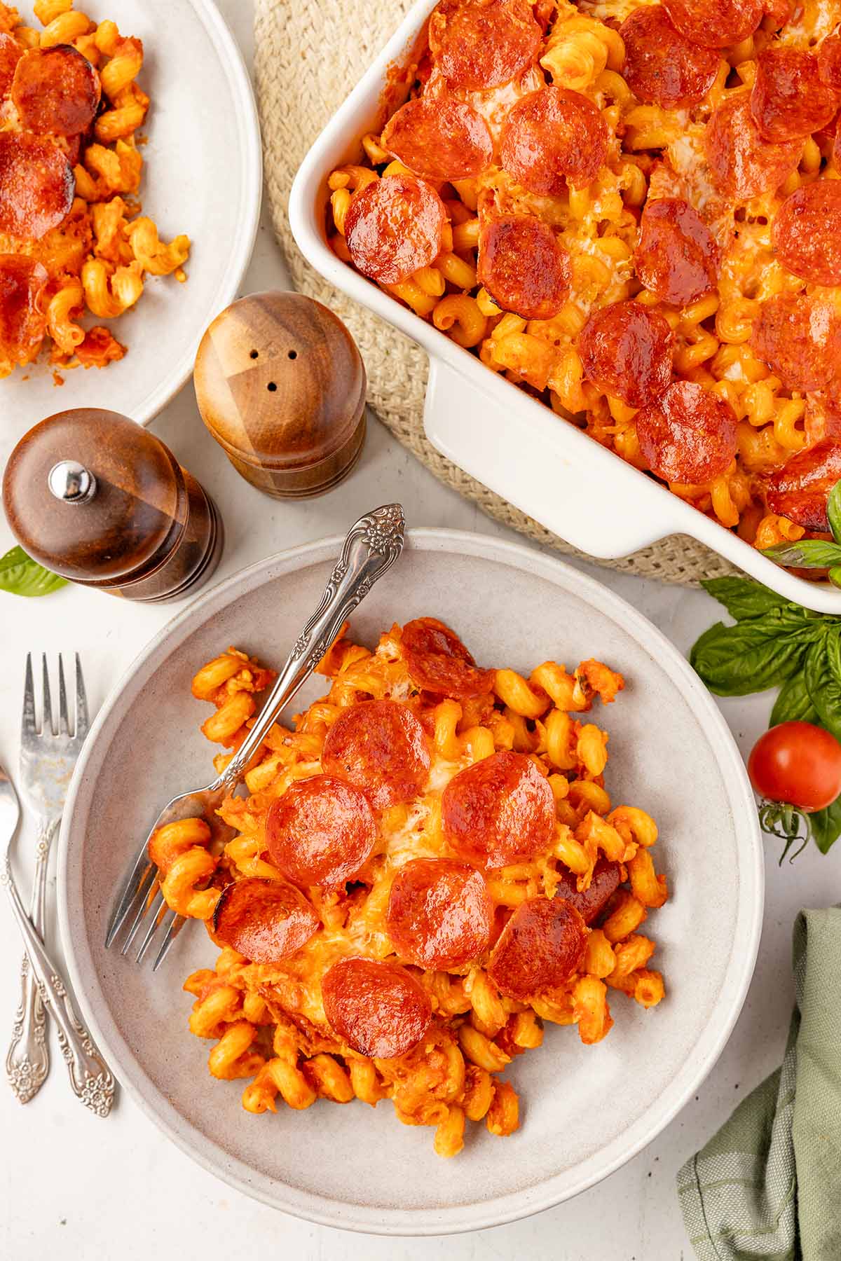 Plated serving of pizza pasta bake next to the full casserole dish on the table.